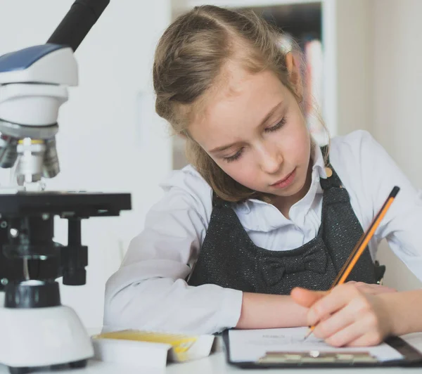 Holčička ve vědě třídě s mikroskopem na stůl. — Stock fotografie