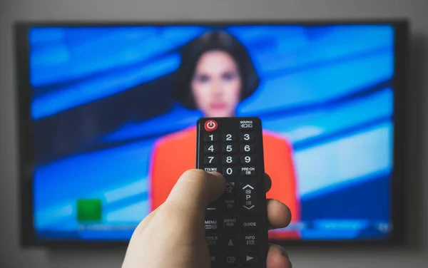 Male hand holding TV remote control. News block.