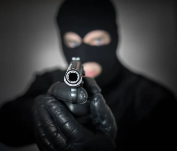 Portrait of armed man in balaclava indoors.