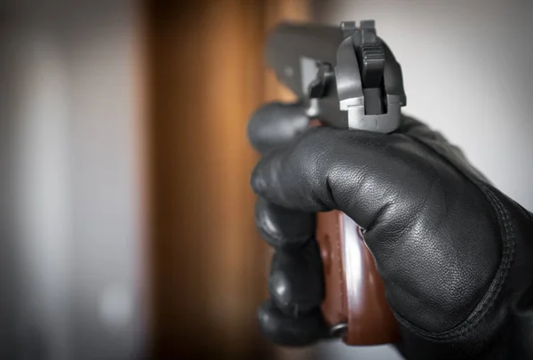 Hand in leather glove holding gun and aiming at the door. — Stock Photo, Image