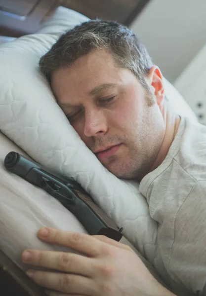 Hombre durmiendo en la cama con un arma cerca de su mano . — Foto de Stock