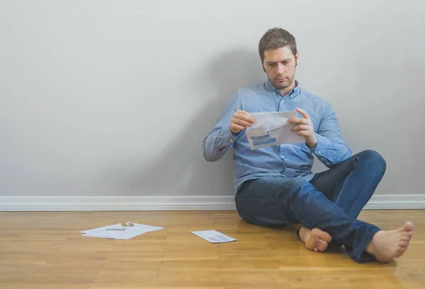 Красивый мужчина сидит на полу и смотрит на свои счета . — стоковое фото