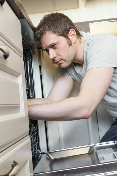 Professional handyman in overalls repairing domestic dishwasher in the kitchen. — Stock Photo, Image