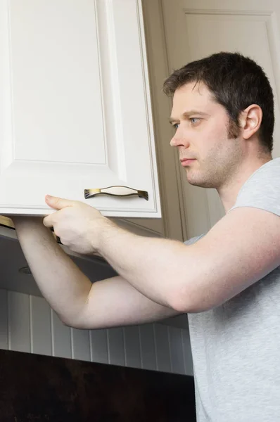 Handyman profissional que instala a porta do armário na cozinha. — Fotografia de Stock