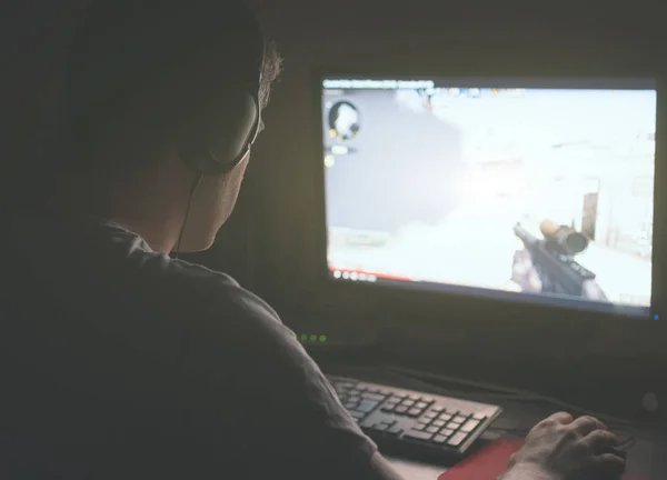 Homem em fones de ouvido jogando jogo de tiro de computador à noite . — Fotografia de Stock