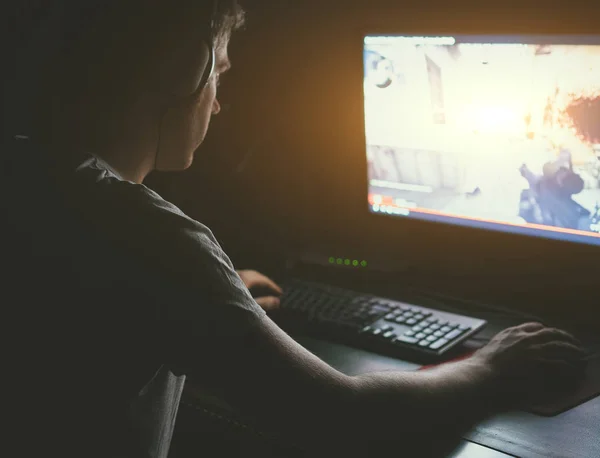 Hombre en auriculares jugando juego de disparos de ordenador en la noche . — Foto de Stock