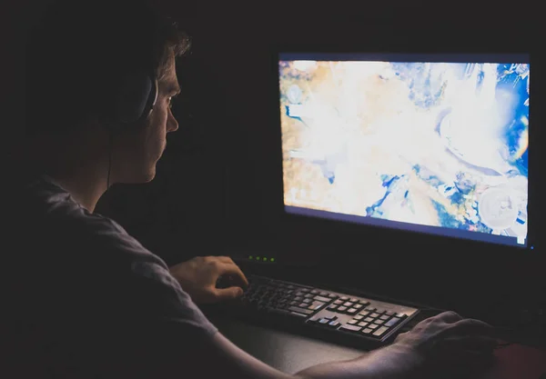 Man in hoofdtelefoons spelen computer strategie game op de nacht. — Stockfoto