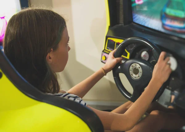 Liten flicka spela racing simulator spel i nöjesparken. — Stockfoto