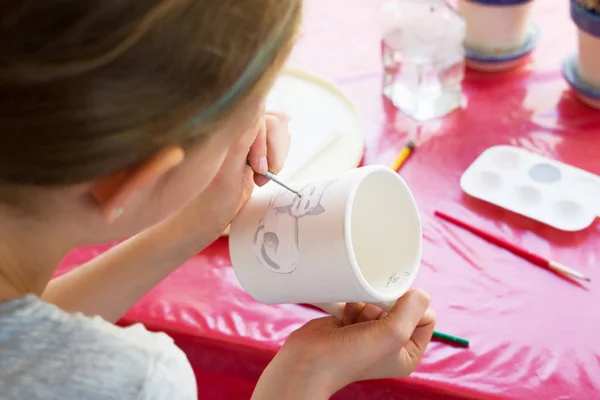 Kind schildert een mok in een pottenbakkerij. — Stockfoto