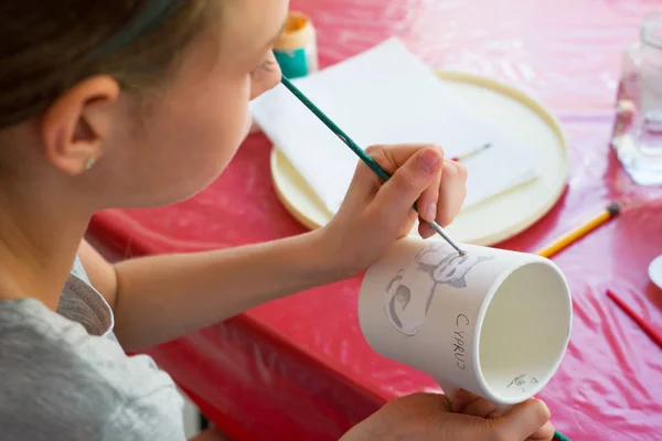 Kind schildert een mok in een pottenbakkerij. — Stockfoto