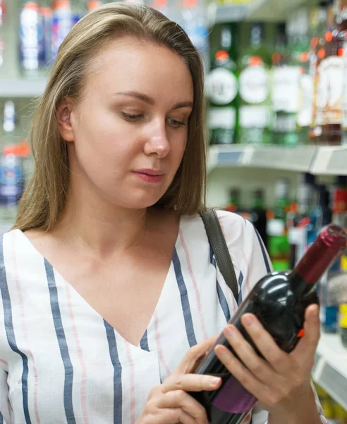 Ładna kobieta wybiera czerwone wino w supermarkecie. — Zdjęcie stockowe