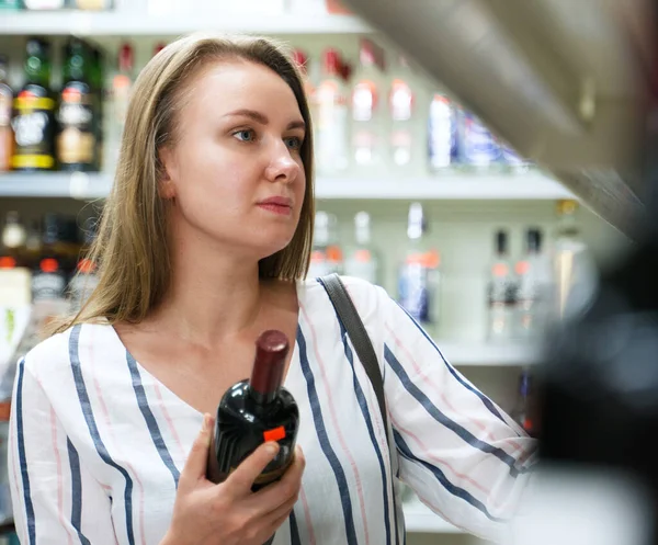 Pretty woman choosing red wine in supermarket. — Stock Photo, Image
