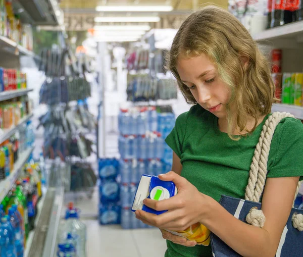 Маленькая девочка выбирает апельсиновый сок в супермаркете . — стоковое фото