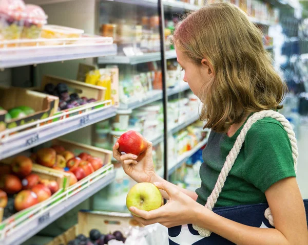 Menina bonita escolhendo maçãs no supermercado . — Fotografia de Stock