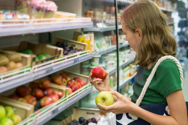 Menina bonita escolhendo maçãs no supermercado . — Fotografia de Stock