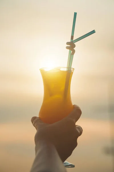 Woman hand is holding fruit cocktail over sunset. — Stock Photo, Image