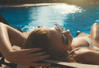 Güneş gözlüklü güzel bayan yazın havuz kenarında güneşleniyor..