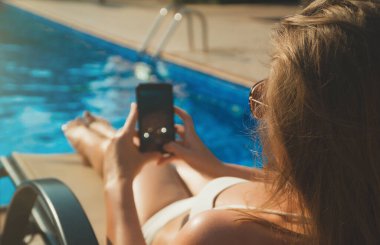Güneş gözlüklü güzel bayan yazın havuz kenarında akıllı telefon kullanıyor..