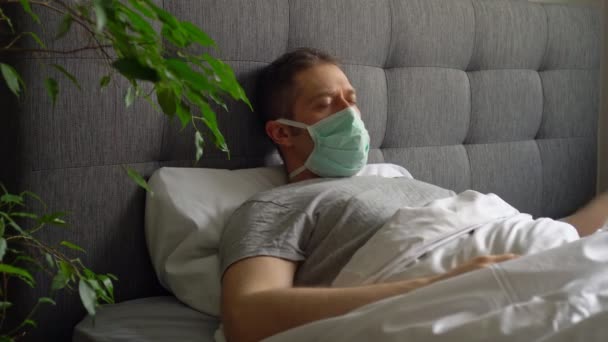 Больной человек в медицинской маске лежит в постели . — стоковое видео