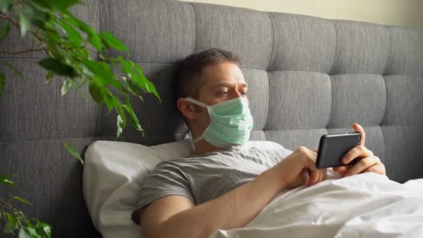 Sick man with medical mask using mobile phone in bed. — Stock Video