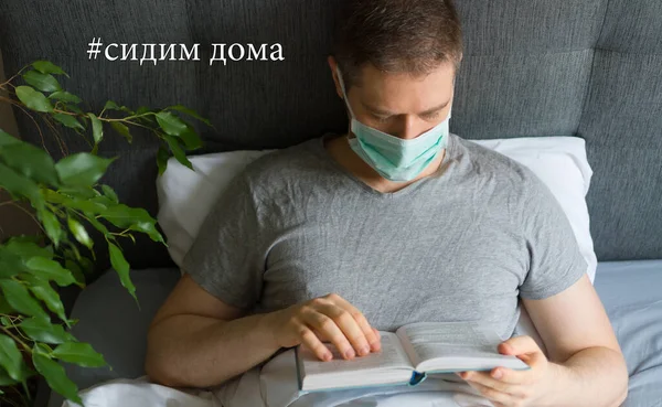 Sick man with medical mask reading book in bed. Stay home in russian language sign.