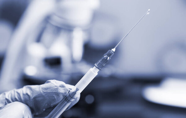 Virologist's hand in glove holding syringe.