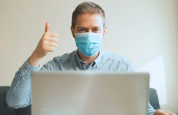 Man in medical mask showing thumbs up via video calling.
