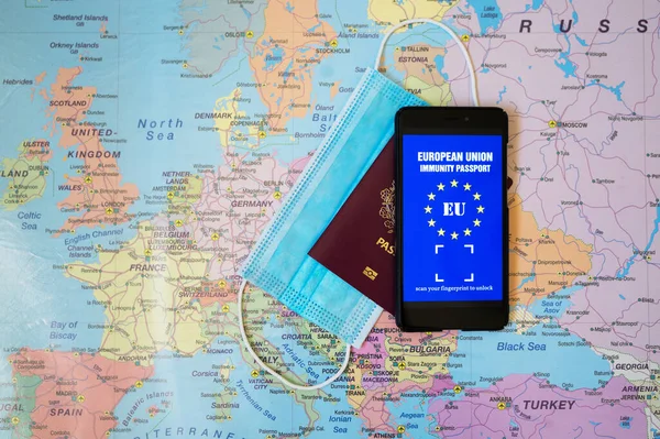 Immunity passport app, Europe Union passport and medical mask on Europe map. Travel during Covid-19 concept.