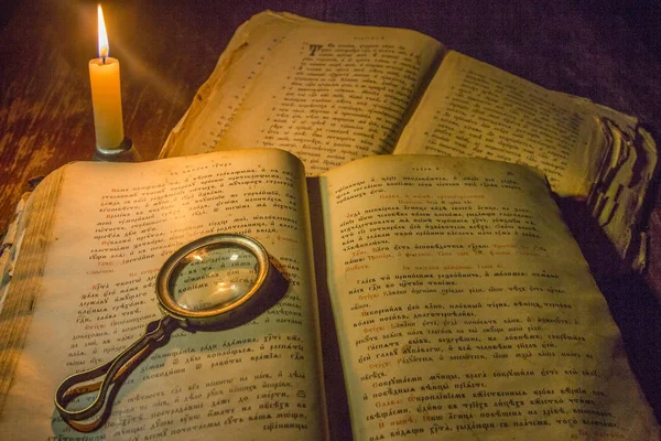 An open ancient prayer books and a magnifying glass on its open pages under the light of a candle