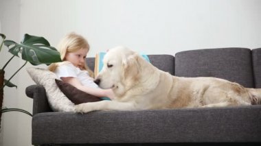 Evcil hayvan bakımı. Sarışın kız köpeğini oturma odasında kanepede yatan bir kitap okuyor. aile içinde mutlu altın geri almak.