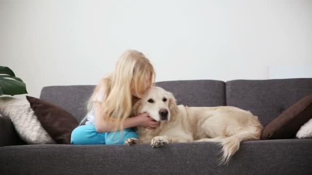 Cuidados para animais de estimação. Uma menina loira acaricia seu cão com amor na sala de estar. feliz golden retriever na família . — Vídeo de Stock
