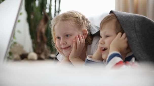 Computers in het leven van de moderne kinderen. kleine broer en zus kijken cartoons op laptop, liggend op bed in de slaapkamer. — Stockvideo