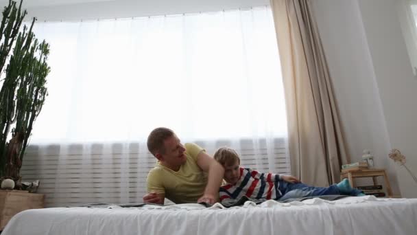 Moderne en gelukkige familie. Vader met een klein zoon is plezier op het bed in de slaapkamer. — Stockvideo
