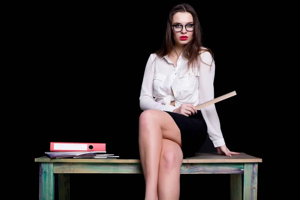Sexy teacher posing on desk in studio on black background Stock Photo