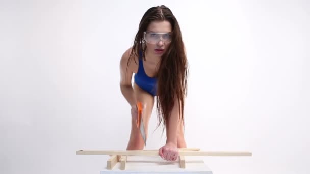 Eine sexy Frau im blauen Badeanzug, die Holzbalken mit Säge zersägt. das schöne Mädchen bewegt sich erotisch. — Stockvideo