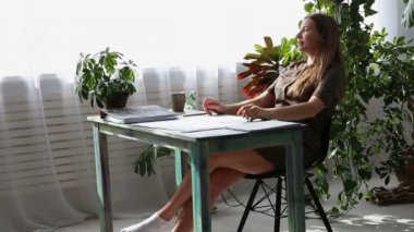 evde çalışıyorum. genç güzel freelancer kadın evde pencere kenarındaki masada çalışıyor. yaşayan bitkiler ile modern ekolojik iç.