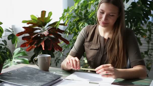 Trabajar en casa. joven hermosa freelancer mujer está trabajando en la mesa por la ventana en la casa. interior ecológico moderno con plantas vivas . — Vídeos de Stock
