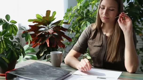 Lavorare a casa. giovane bella donna freelancer sta lavorando al tavolo dalla finestra in casa. interni ecologici moderni con piante vive . — Video Stock