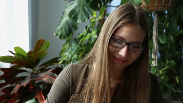 Werk thuis. mooie jongedame werkt aan de tafel bij het raam in het huis - close-up. moderne ecologische interieur met levende planten. — Stockvideo