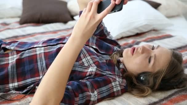 现代青年生活中的电子设备。年轻女孩在家用手机在床上休息. — 图库视频影像