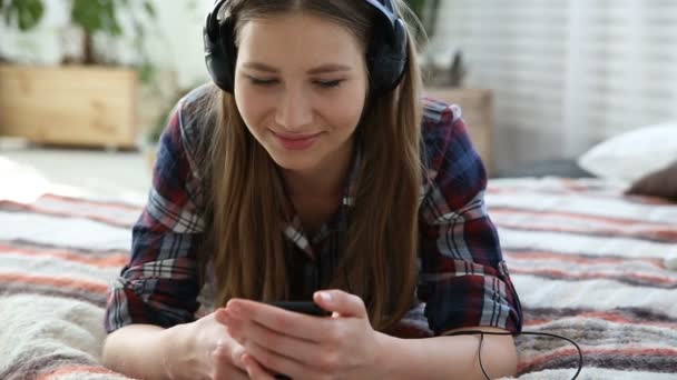 Dispositivos electrónicos en la vida de la juventud moderna. joven adolescente descansando en casa en la cama con teléfono móvil . — Vídeos de Stock