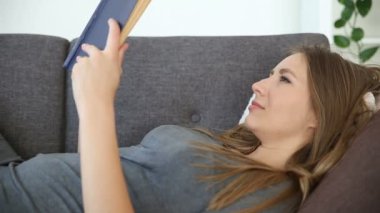 Avrupa görünümlü kız bir kitap okur ev ev gri bir kanepe oturma odasında