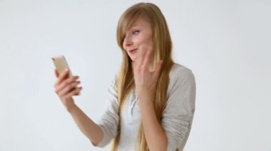 Modern gençlik. Avrupa görünümü ile anlamlı bir şekilde beyaz duvarının yakınında bir video iletişimi smartphone cep telefonu ile konuşurken sarışın güzel uzun saçlı kız