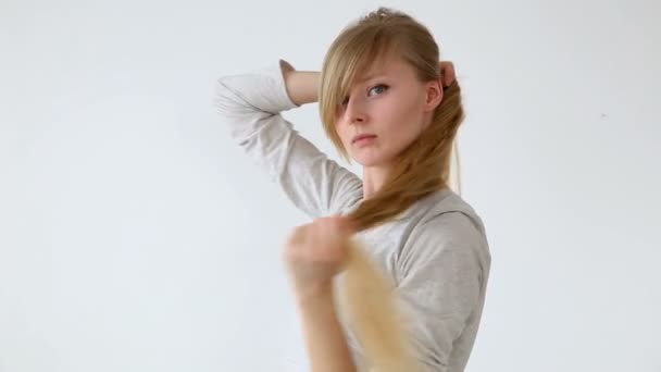 Красивая длинноволосая девушка европейского образца с светлыми волосами, делающая различные прически на белом фоне — стоковое видео