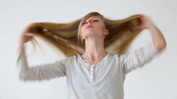 Schöne langhaarige Mädchen von europäischem Aussehen mit blonden Haaren machen verschiedene Frisuren auf weißem Hintergrund — Stockvideo