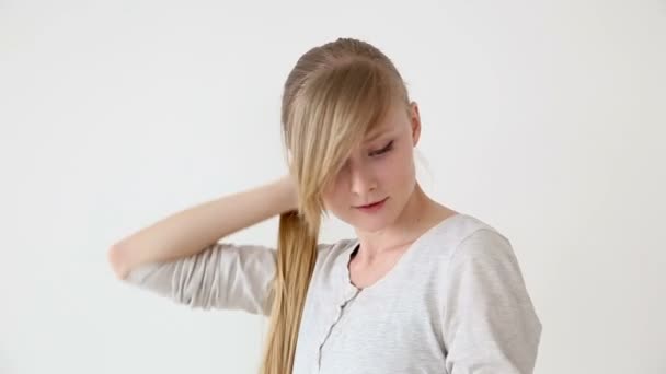 Hermosa chica de pelo largo de apariencia europea con cabello rubio haciendo diferentes peinados sobre fondo blanco — Vídeos de Stock