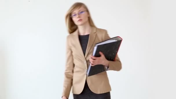 Νεαρή όμορφη γυναίκα στο επιχειρηματικό στυλ με τα γυαλιά και έγγραφα στα χέρια θέτοντας κοντά στο λευκό φόντο — Αρχείο Βίντεο