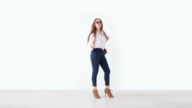 moda modern gençlik. şık kız kot pantolon, beyaz gömlek, deri sırt çantası ve gözlük ile beyaz duvara poz.