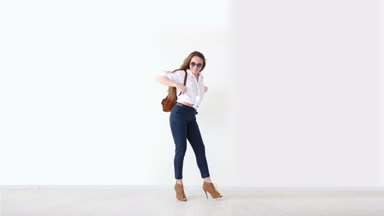 moda modern gençlik. şık kız kot pantolon, beyaz gömlek, deri sırt çantası ve gözlük ile beyaz duvara poz.