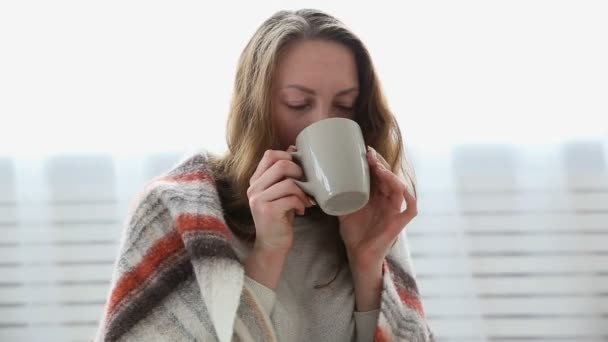 Een eenvoudige vrouw drinkt thee verpakt in een warme wollen deken — Stockvideo